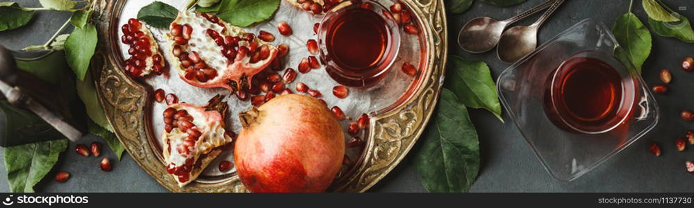 Cups of Pomegranate tea and fresh pomegranates on dark background, flat lay