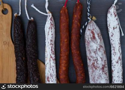 Cured meat and sausages hanging on black wooden background close up. Cured meat and sausages