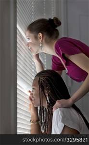 Curious teenage girls are looking through a window blind