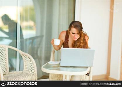 Curious young woman with cup of tea looking in laptop&#xA;