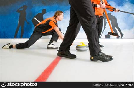 Curler, gliding on the ice, delivering a stone, with two sweepers, to act on the Skip&rsquo;s request