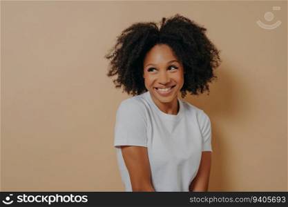 Curly African woman in white shirt, shy smile, positive emotions. Face expressions concept.