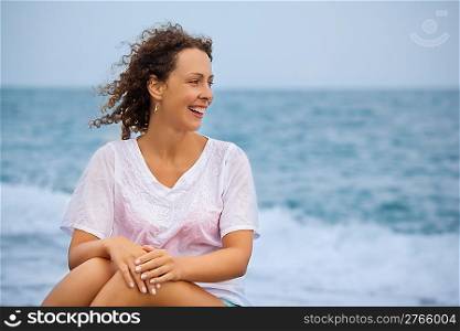 Curly beautiful young woman sitting near sea in evening, Looking afar