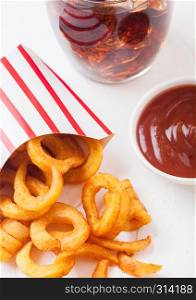 Curly fries fast food snack in paper container with glass of cola and ketchup on kitchen background. Unhealthy junk food