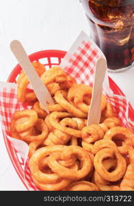 Curly fries fast food snack in red plastic tray with glass of cola on kitchen background. Unhealthy junk food