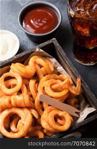Curly fries fast food snack in wooden box with ketchup and glass of cola on kitchen background. Unhealthy junk food