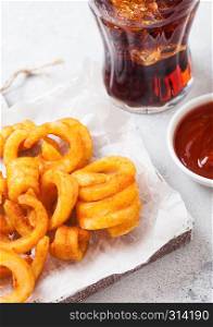 Curly fries fast food snack on wooden board with ketchup and glass of cola on kitchen background. Unhealthy junk food