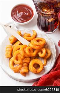 Curly fries fast food snack on wooden board with ketchup and glass of cola on kitchen background. Unhealthy junk food