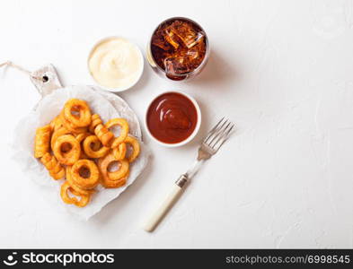 Curly fries fast food snack on wooden board with ketchup and glass of cola on kitchen background. Unhealthy junk food