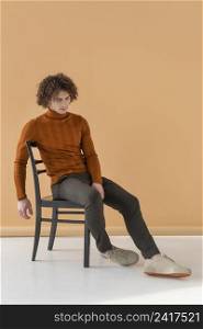 curly haired man with brown blouse posing chair