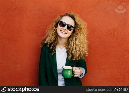 Curly-haired woman, sunglasses, jacket, cappuccino, smile, orange wall.. Curly-haired woman, sunglasses, jacket, cappuccino, smile, orange wall. 