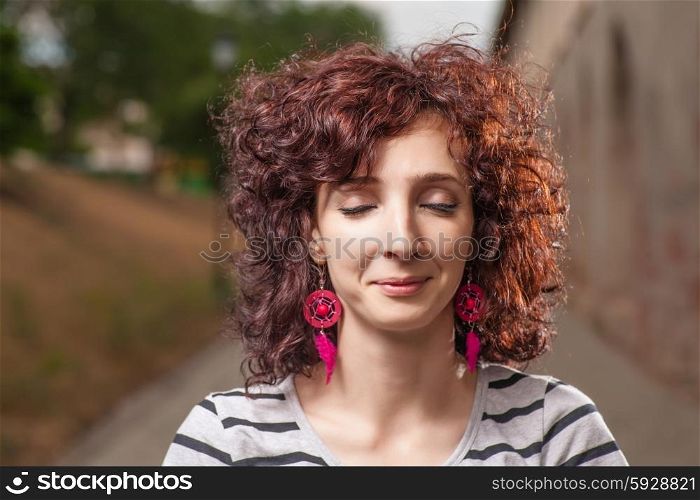 Curly haired women outdoors with her eyes closed. Pretty smile.
