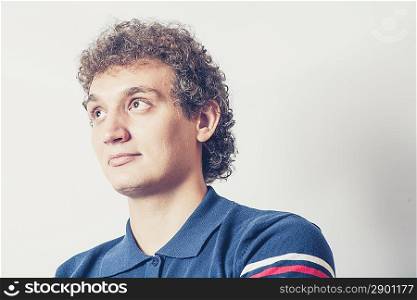 Curly haired young man on gray background with pensive expression.