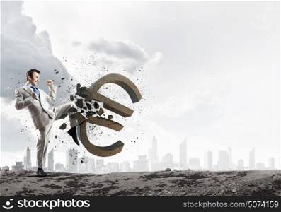 Currency concept. Businessman breaking stone euro symbol with karate kick