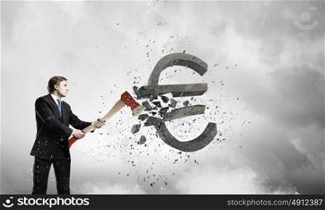 Currency concept. Young determined businessman crashing euro sign with axe