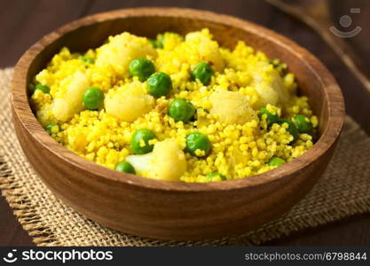 Curried couscous with peas, cauliflower, ginger and garlic served in wooden bowl, photographed with natural light (Selective Focus, Focus in the middle of the dish)
