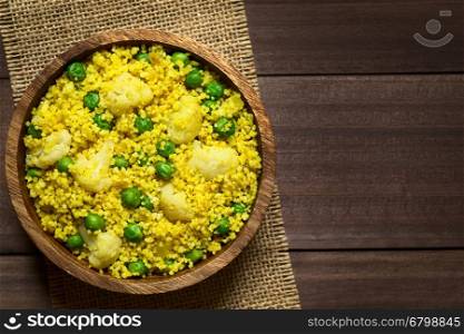 Curried couscous with peas, cauliflower, ginger and garlic served in wooden bowl, photographed overhead on dark wood with natural light (Selective Focus, Focus on the top of the dish)