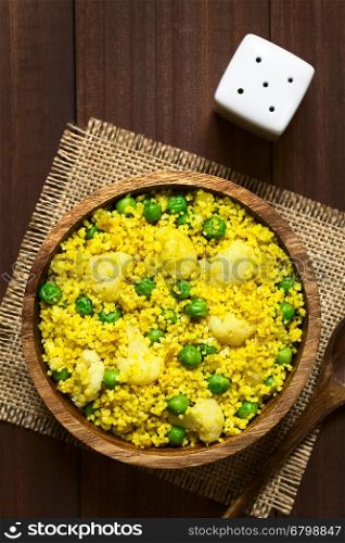 Curried couscous with peas, cauliflower, ginger and garlic served in wooden bowl, photographed overhead on dark wood with natural light (Selective Focus, Focus on the top of the dish)