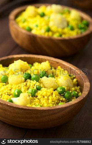 Curried couscous with peas, cauliflower, ginger and garlic served in wooden bowls, photographed with natural light (Selective Focus, Focus in the middle of the first dish)