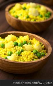 Curried couscous with peas, cauliflower, ginger and garlic served in wooden bowls, photographed with natural light (Selective Focus, Focus in the middle of the first dish)