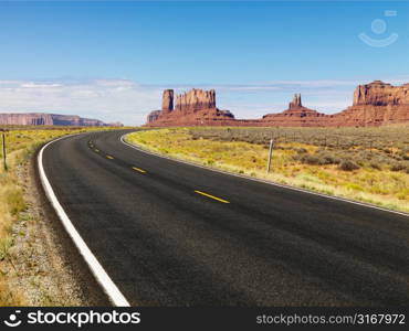 Curve in road in scenic desert road with mesa land formations and mountains.