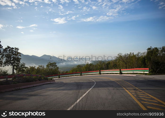 curve road driving a car on mountain road downhill / Dramatic curve beautiful blue sky cloud with mist fog in the morning and forest tree on the roadside at countryside