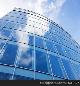 curved facade of modern glass blue office and sky with clouds reflected