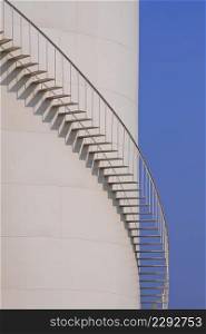 Curved line of spiral staircase on oil storage fuel tank with blue sky in vertical frame