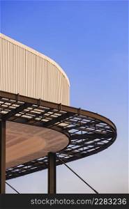 Curved metal awning structure with corrugated steel roof of modern building in construction site against blue sky in vertical frame