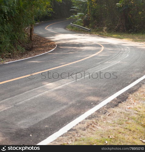 Curvy road down the hill. Road curving down from the mountain. There are more trees on either side of the road.