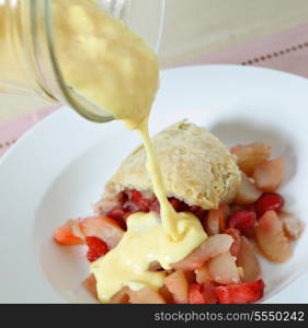 Custard being poured on a traditional British steamed fruit pudding, of pears and strawberries with a sweet suet pastry crust