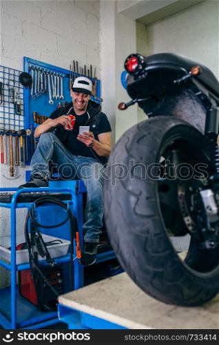 Custom motorcycles mechanic resting having a beer in his workshop. Motorcycles mechanic resting having a beer