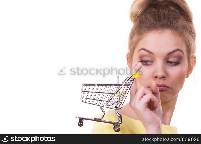 Customer buying in shop. Unhappy thinking woman holding small tiny shopping cart trolley about to buy products having doubts.. Woman holding shopping cart