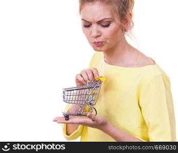 Customer buying in shop. Unhappy thinking woman holding small tiny shopping cart trolley about to buy products having doubts.. Woman holding shopping cart