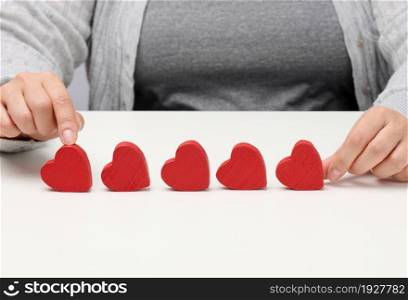 Customer experience feedback concept. Five red hearts, the best rating of excellent services with a female hand to meet. White table