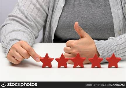 Customer experience feedback concept. Five red stars, the best rating of excellent services with a female hand to meet. White table