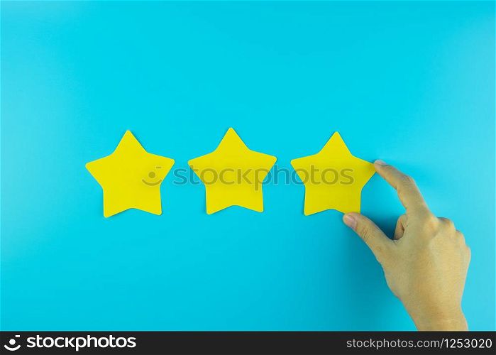 customer holding three star yellow paper note on blue background. Customer reviews, feedback, rating, ranking and service concept.