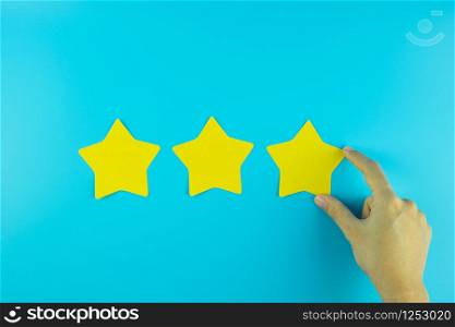 customer holding three star yellow paper note on blue background. Customer reviews, feedback, rating, ranking and service concept.