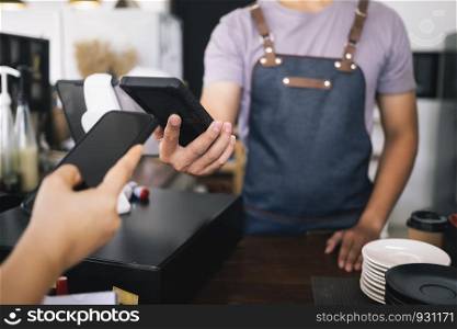 Customer making payment using NFS technology at coffee cafe. Small business owner and contactless or wireless payment concept.