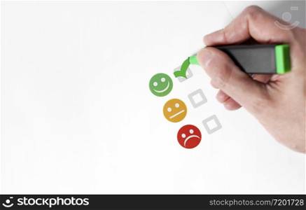 Customer satisfaction happy feedback rating checklist and excellent business quality evaluation concept with a customer hand checking a green smiling emoticon face icon top view with white copy space.