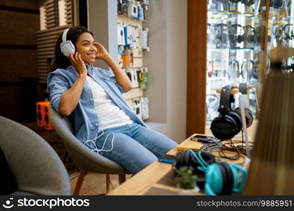 Customer trying on headphones in audio store, music fan. Female person in music shop, showcase with earphones on background, buyer in multimedia salon. Customer trying on headphones in audio store