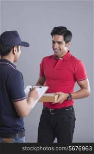 Customer with package looking at delivery man against gray background
