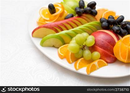 cut apples and oranges with grapes on oval plate, shallow DOF