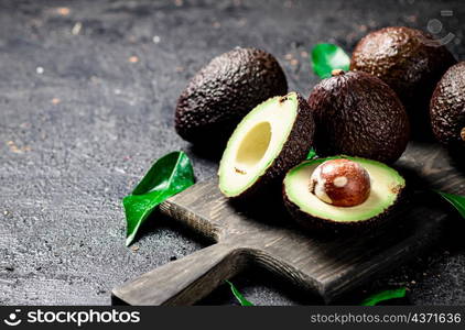 Cut avocado with leaves on a cutting board. On a black background. High quality photo. Cut avocado with leaves on a cutting board.