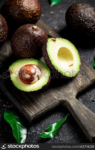 Cut avocado with leaves on a cutting board. On a black background. High quality photo. Cut avocado with leaves on a cutting board.