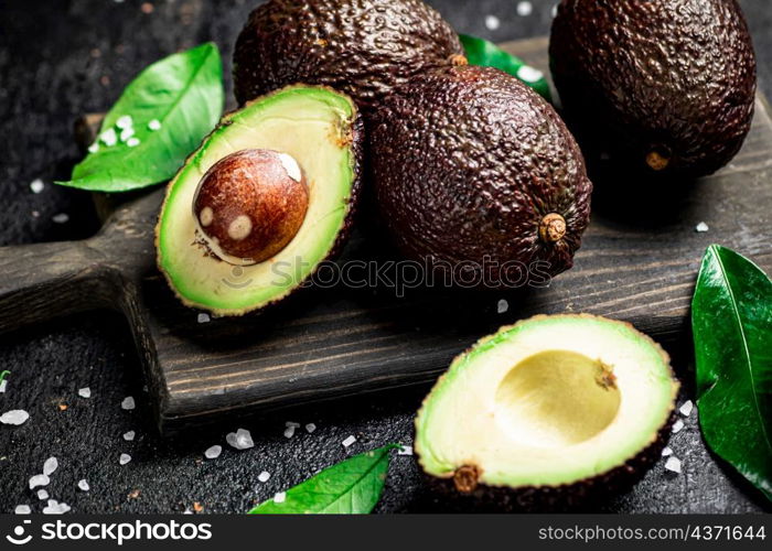 Cut avocado with leaves on a cutting board. On a black background. High quality photo. Cut avocado with leaves on a cutting board.