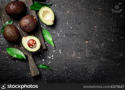Cut avocado with leaves on a cutting board. On a black background. High quality photo. Cut avocado with leaves on a cutting board.