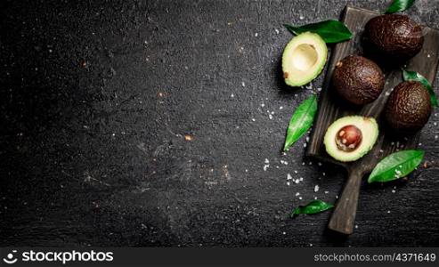 Cut avocado with leaves on a cutting board. On a black background. High quality photo. Cut avocado with leaves on a cutting board.