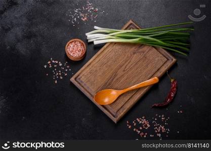 Cut Green onions chives on a cutting board. Dark wooden background. Top view of spring onions bunch ready to cutting on chopping board
