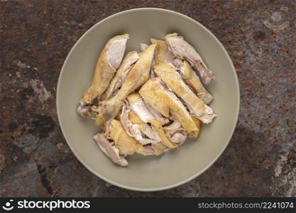 cut of boiled chicken in simply ceramic plate on rusty texture background, top view, flat lay